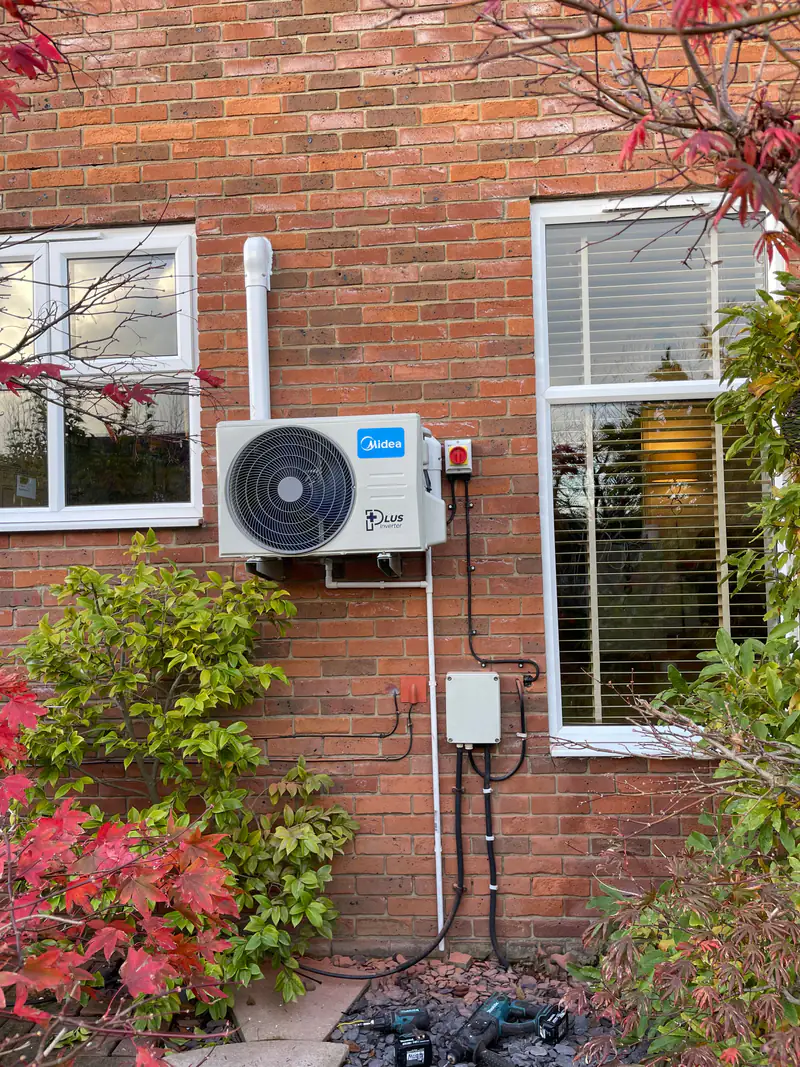 Neatly installed outdoor air conditioning unit Outdoor air conditioning unit wall-mounted on brickwork beside a garden shrub at a York house